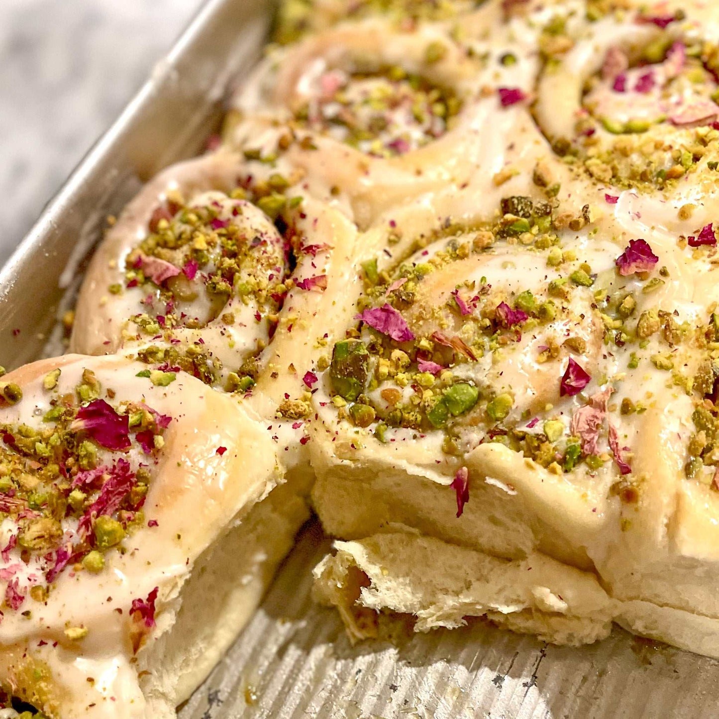Rose and pistachio cinnamon buns with rose icing and chopped pistachios in a box of four