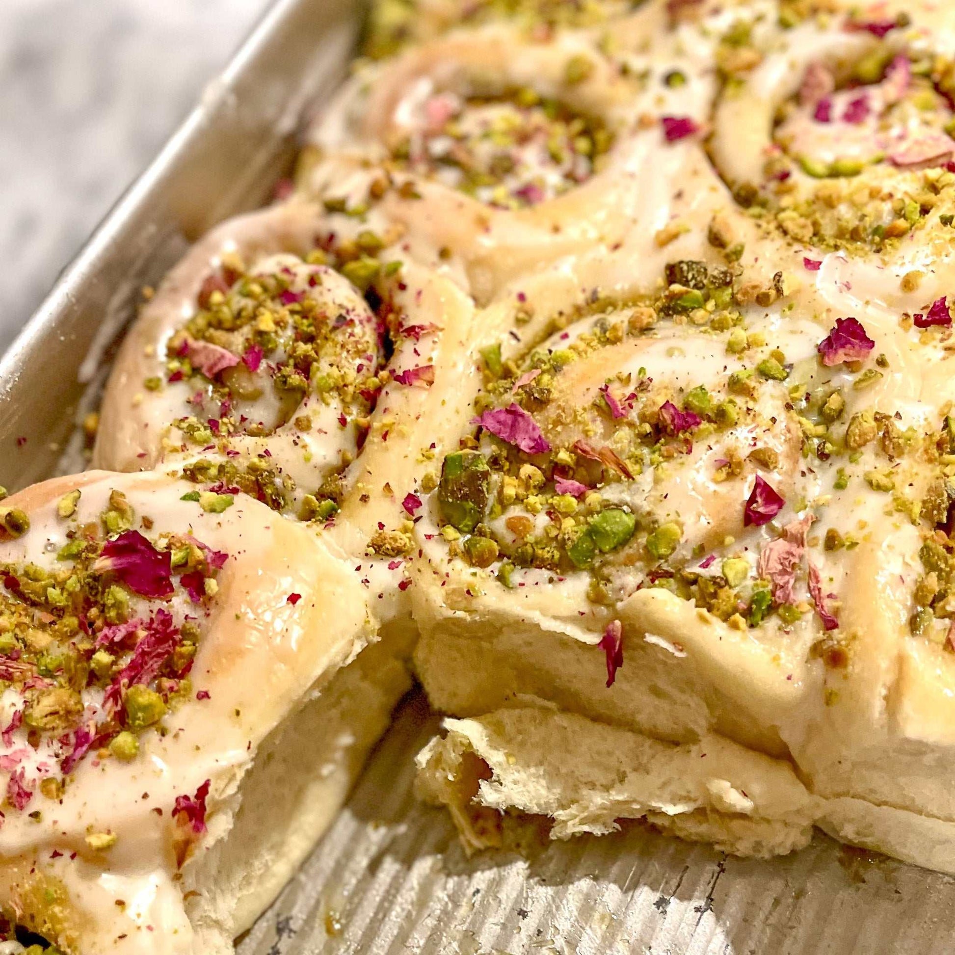 Rose and pistachio cinnamon buns with rose icing and chopped pistachios in a box of four