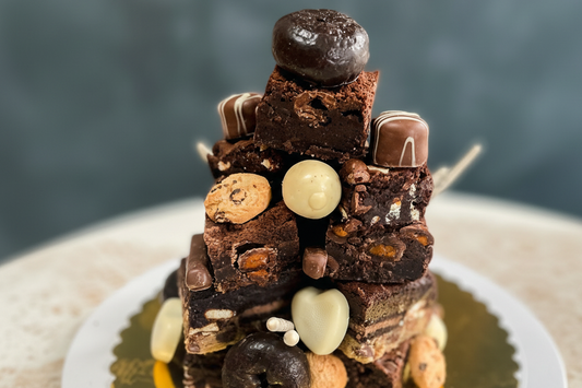Three-layer brownie tower with vanilla frosting and chocolate ganache topped with candy and cookies